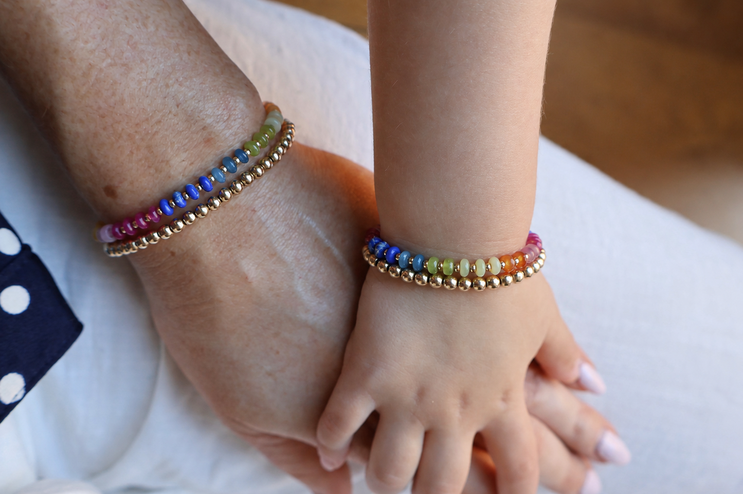 Close-up of hands wearing colorful beaded bracelets on a neutral background