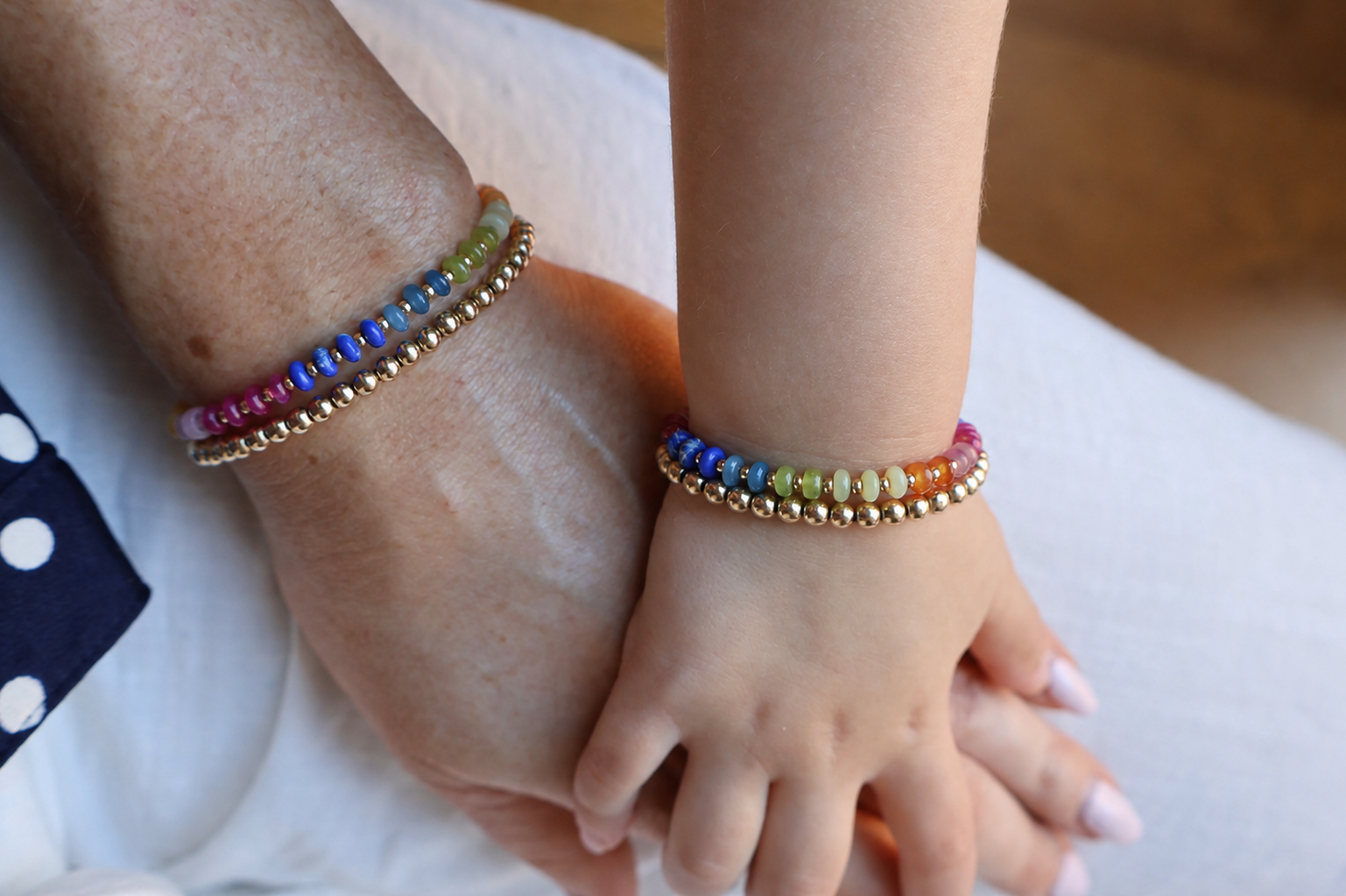 Close-up of hands wearing colorful beaded bracelets on a neutral background